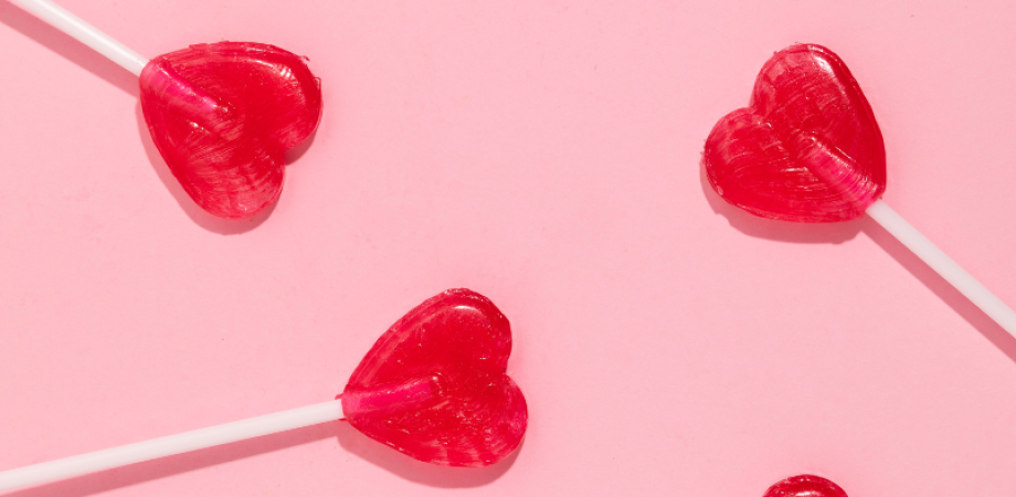 Drie rode lolly's in de vorm van een hartje op roze achtergrond