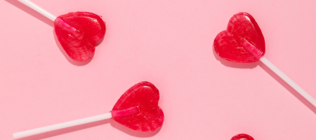 Drie rode lolly's in de vorm van een hartje op roze achtergrond